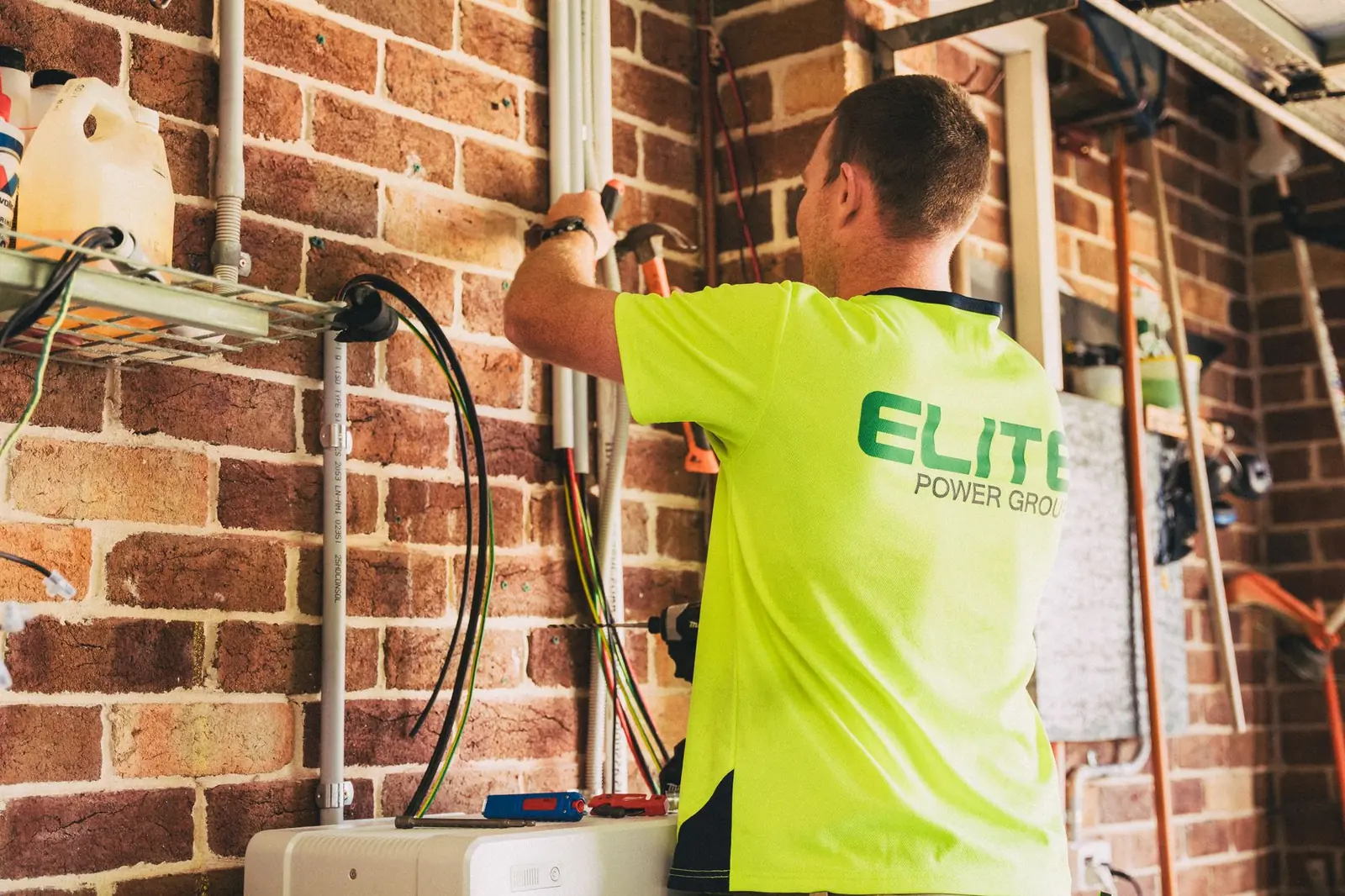 Électricien en t-shirt fluo raccordant des câbles sur un mur de briques