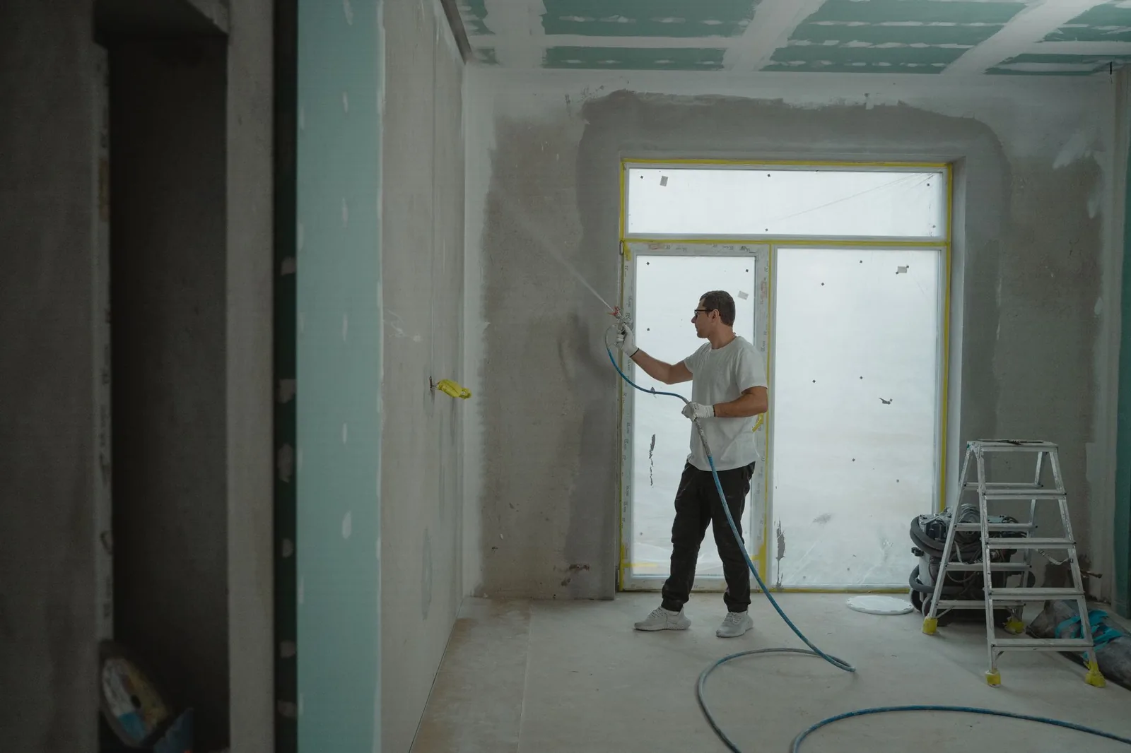 Ouvrier intervenant sur une grande baie vitrée dans un logement en travaux