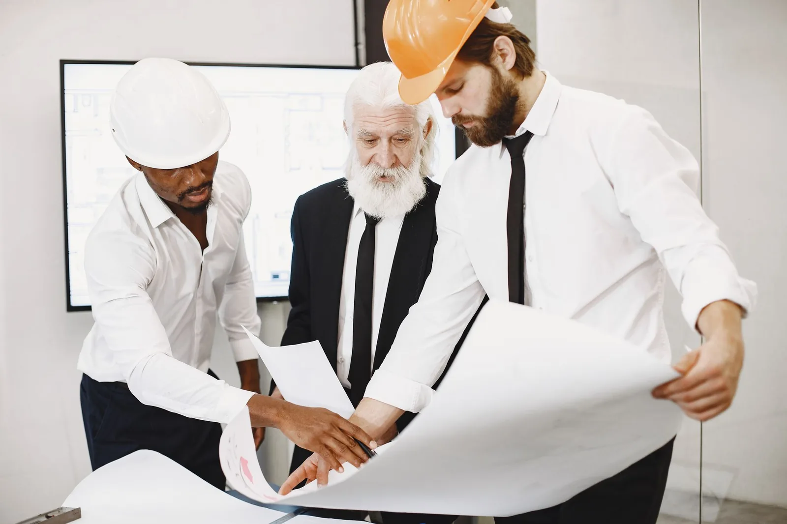 Trois hommes en casque de chantier examinent un plan déroulé sur une table