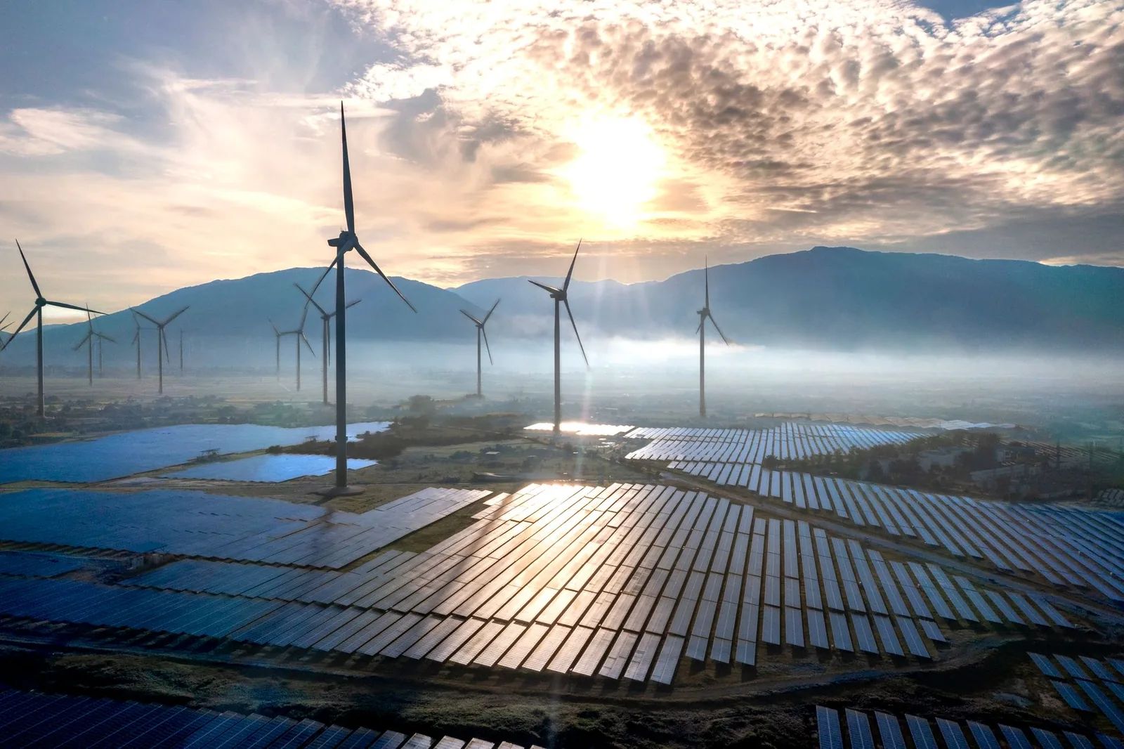 Champ de panneaux solaires au sol et éoliennes au lever du soleil