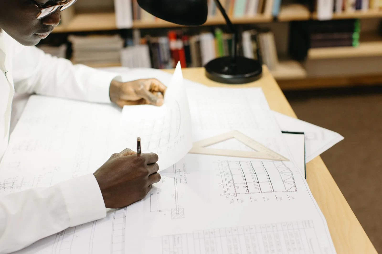 Technicien annotant au crayon des plans de bâtiment sur un bureau