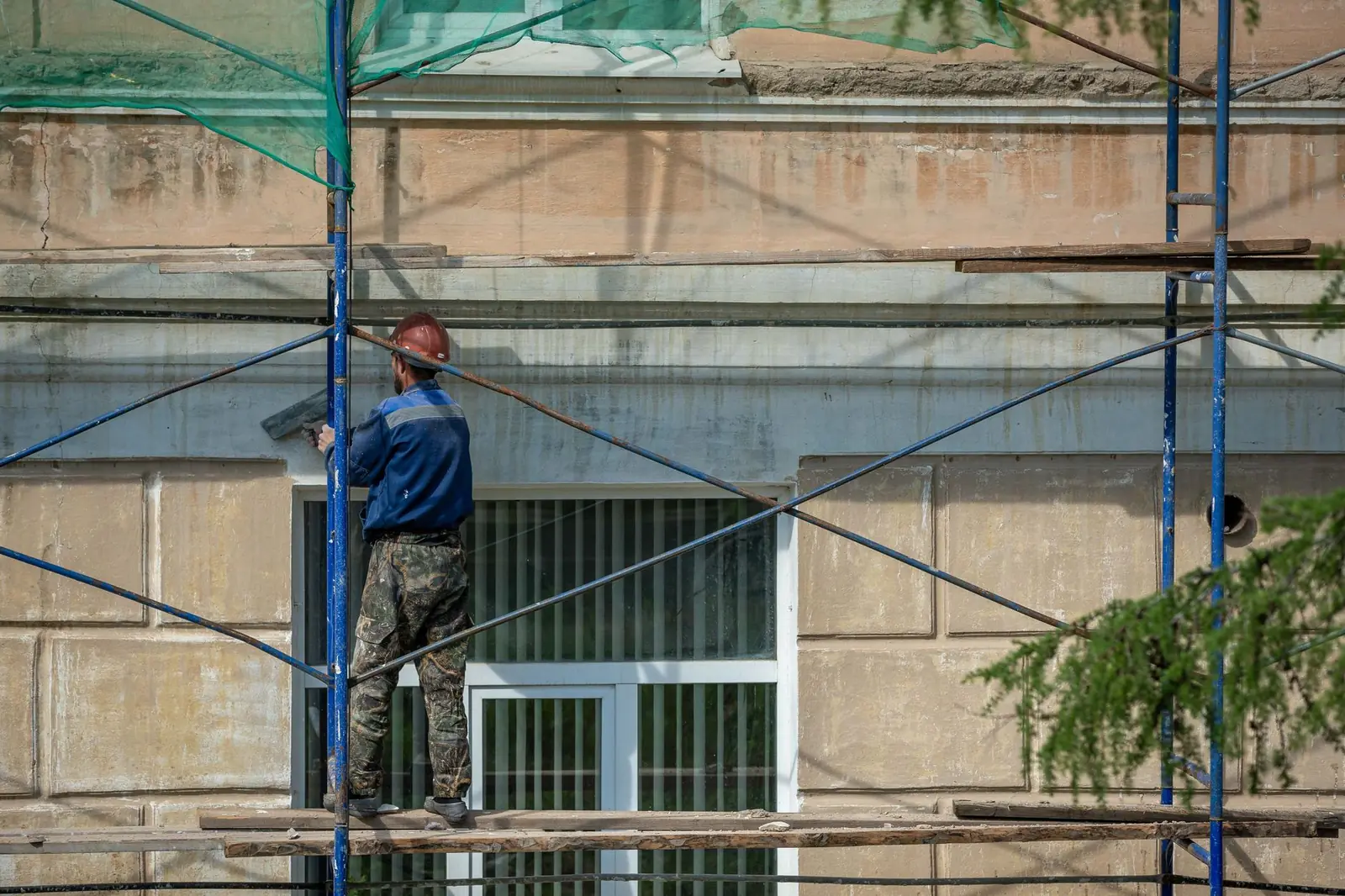 Ouvrier sur un échafaudage enduisant la façade d'un bâtiment