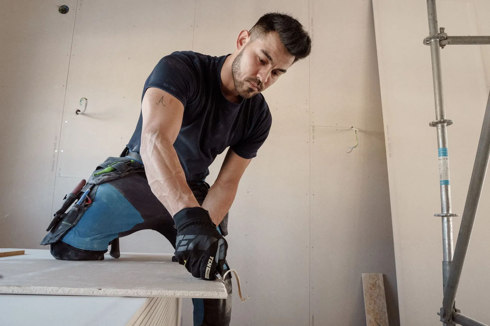 Ouvrier ganté agenouillé manipulant une plaque de plâtre sur un chantier intérieur