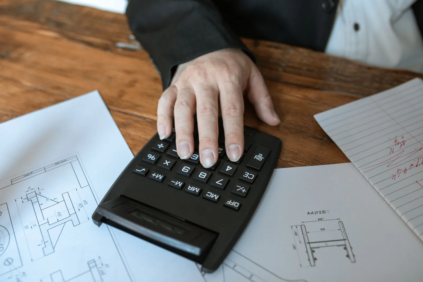 Main appuyant sur une calculatrice posée sur des plans techniques