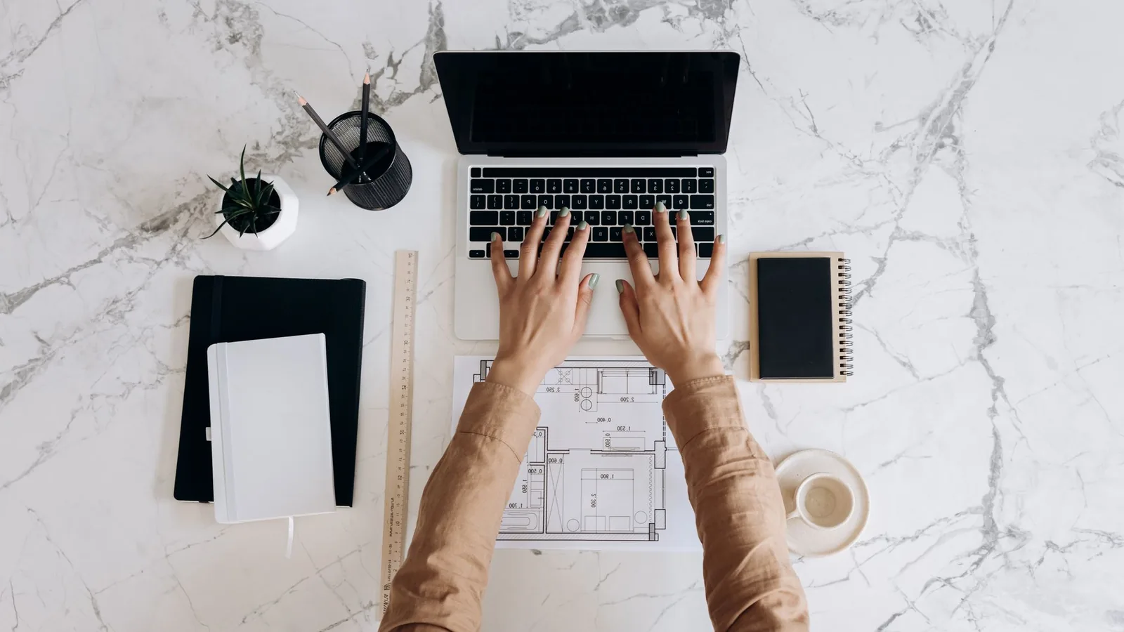 Mains d'une femme tapant sur un ordinateur portable posé sur un plan d'architecte