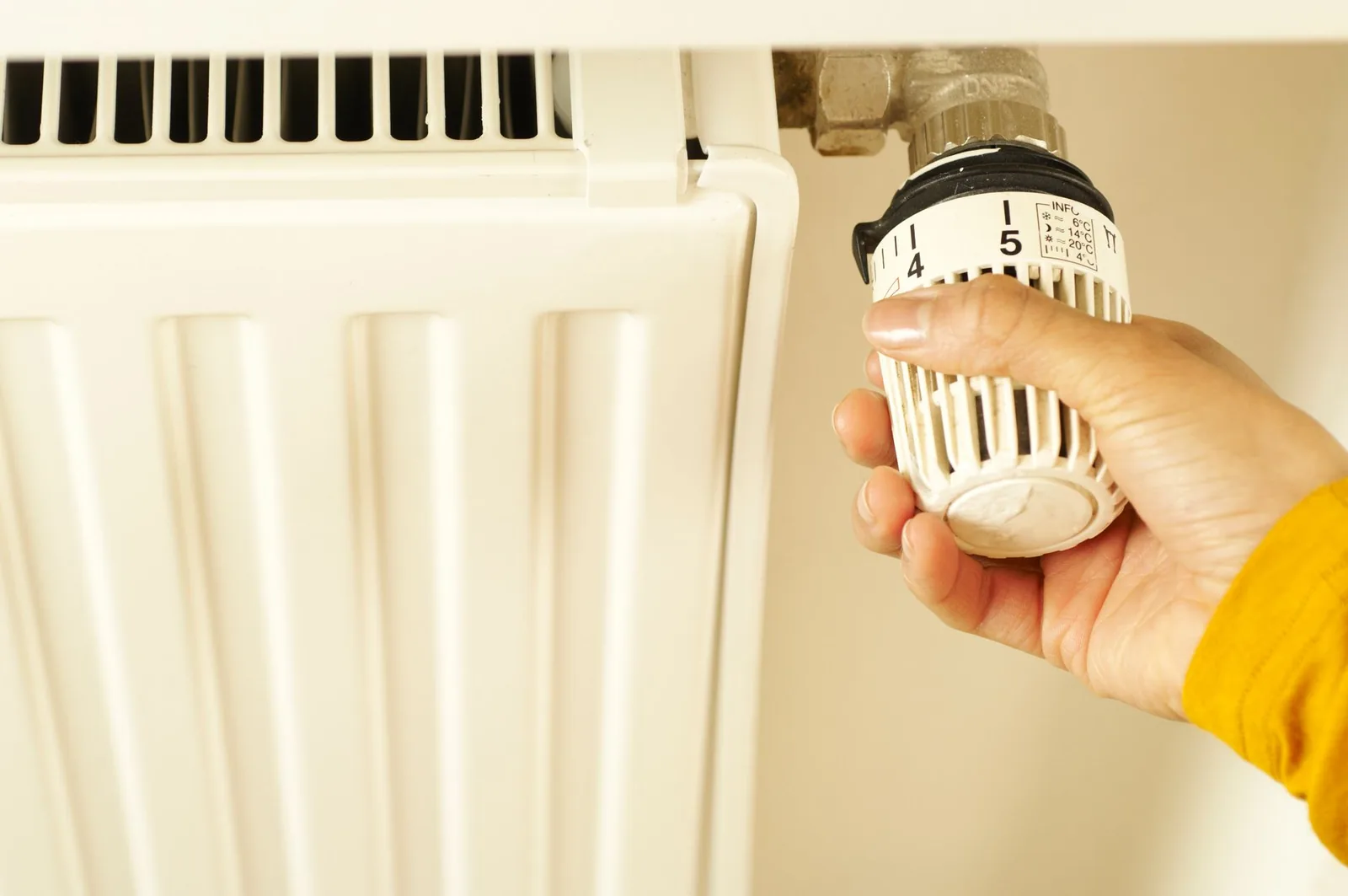 Main réglant la tête thermostatique graduée d'un radiateur blanc mural