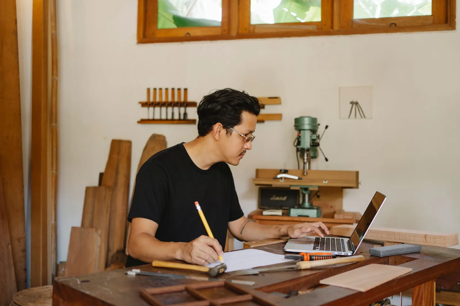 Menuisier prenant des notes devant un ordinateur portable dans son atelier