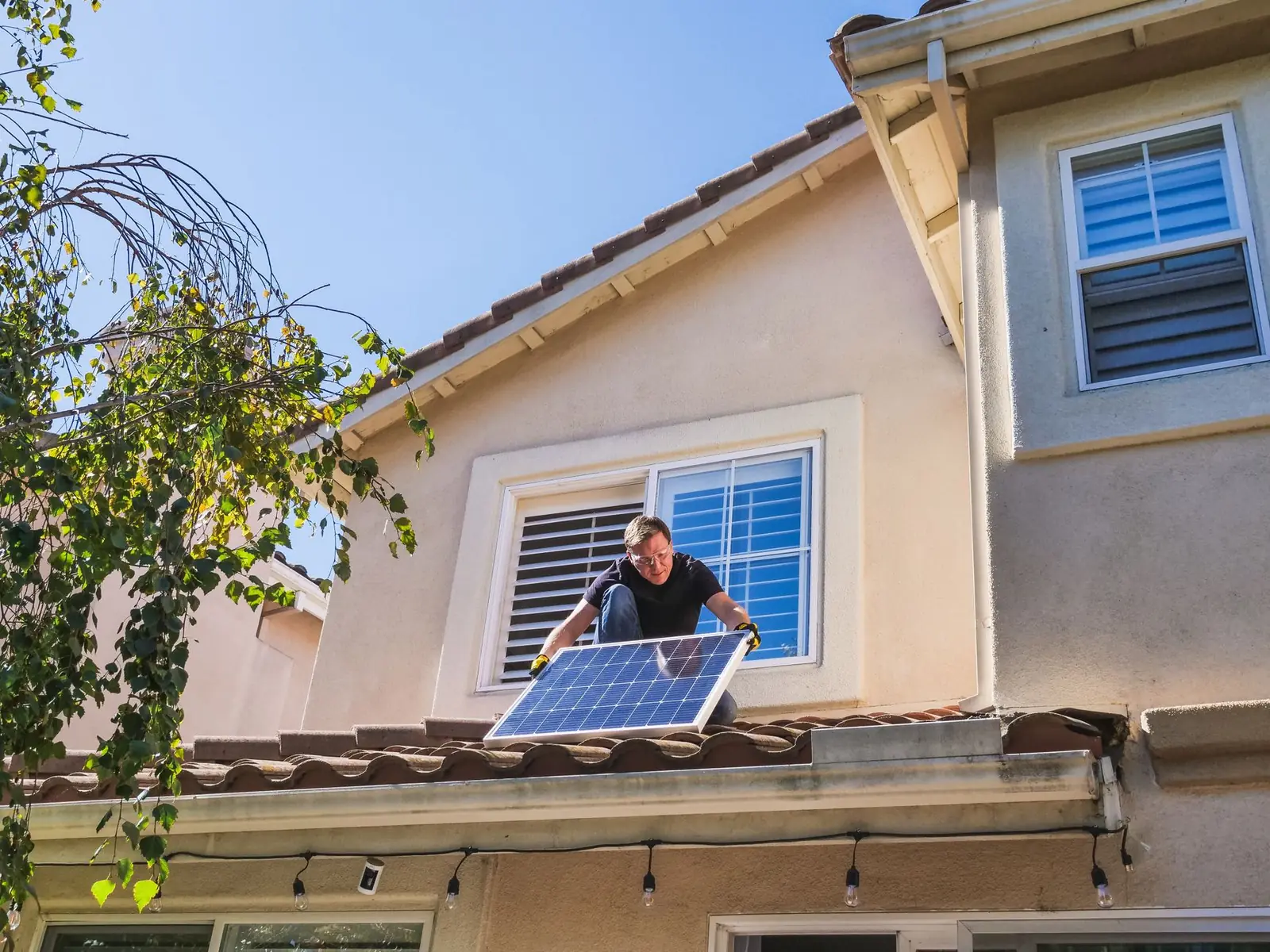 Homme installant un panneau solaire sur la toiture en tuiles d'une maison