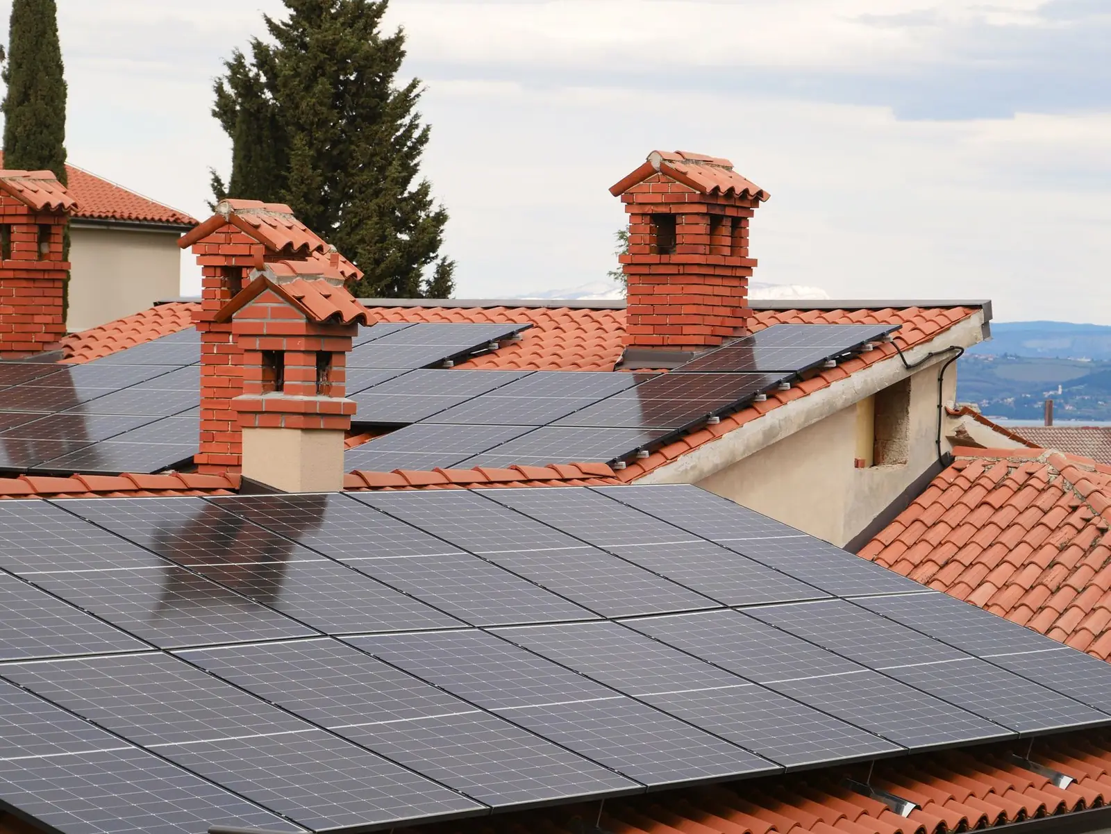 Panneaux solaires posés sur des toitures en tuiles rouges entre deux cheminées en briques