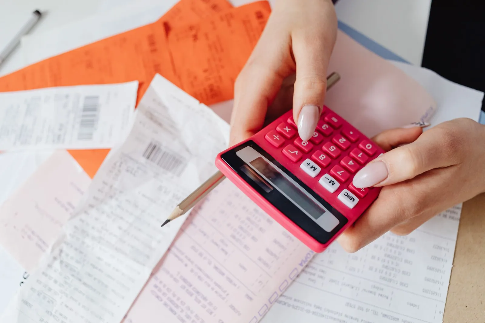 Mains tenant une calculatrice rouge au-dessus de tickets de caisse et factures