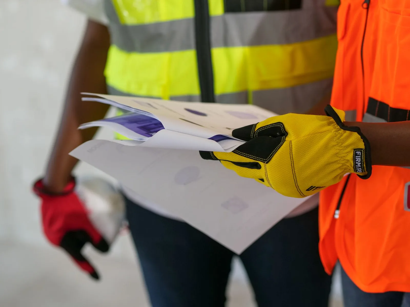 Ouvrier ganté en gilet de chantier consultant des plans avec un collègue