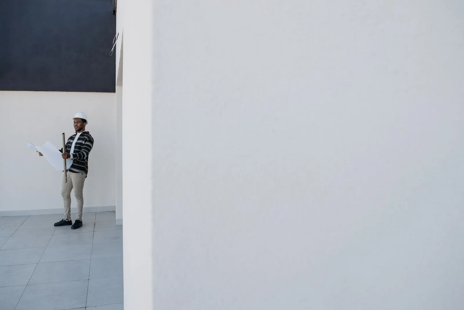 Homme casqué tenant un plan roulé dans un local vide en chantier