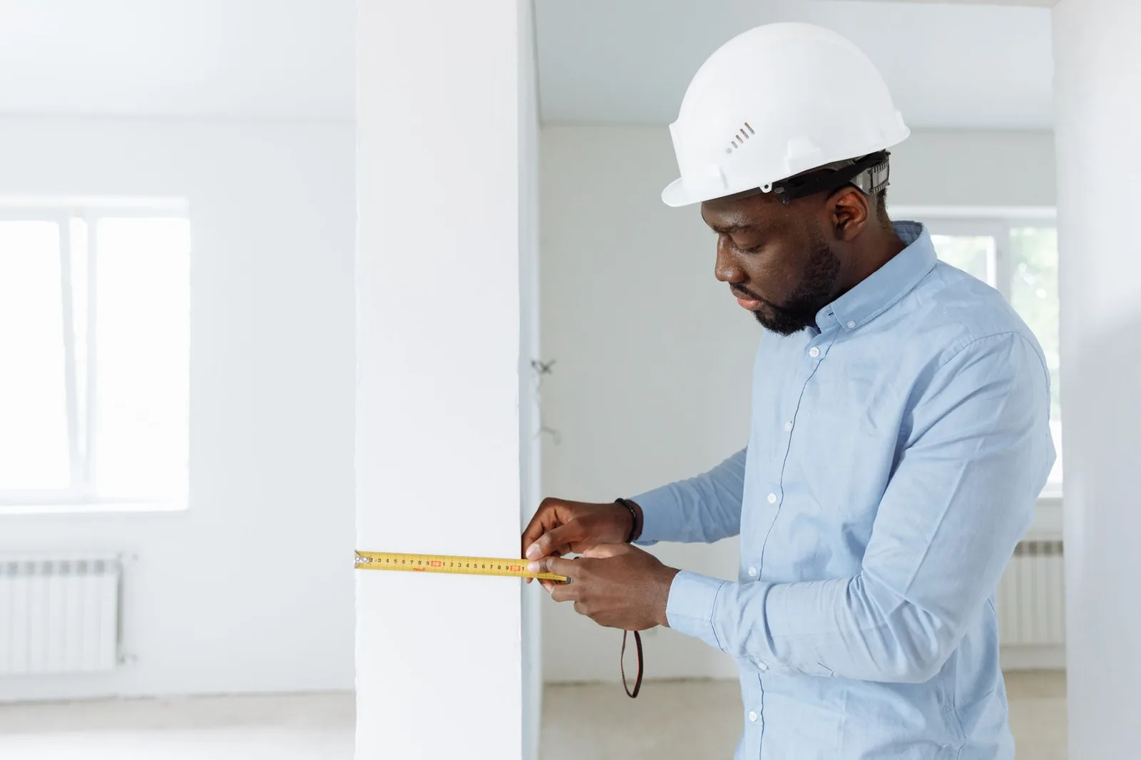 Artisan mesurant un mur au mètre ruban sur un chantier de rénovation