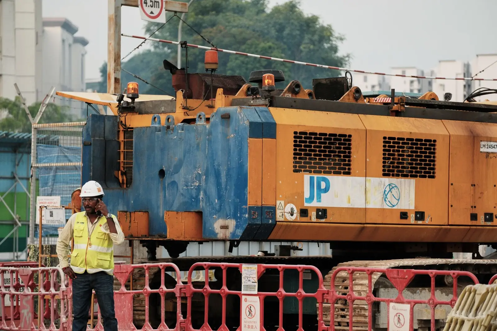 Ouvrier casqué en gilet jaune au téléphone devant un engin de chantier