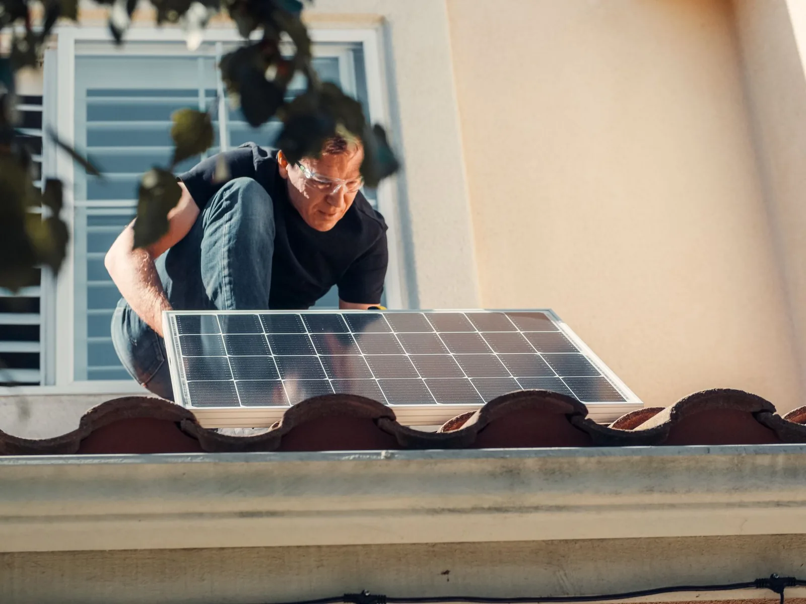 Installateur à lunettes de protection posant un panneau solaire sur un toit en tuiles