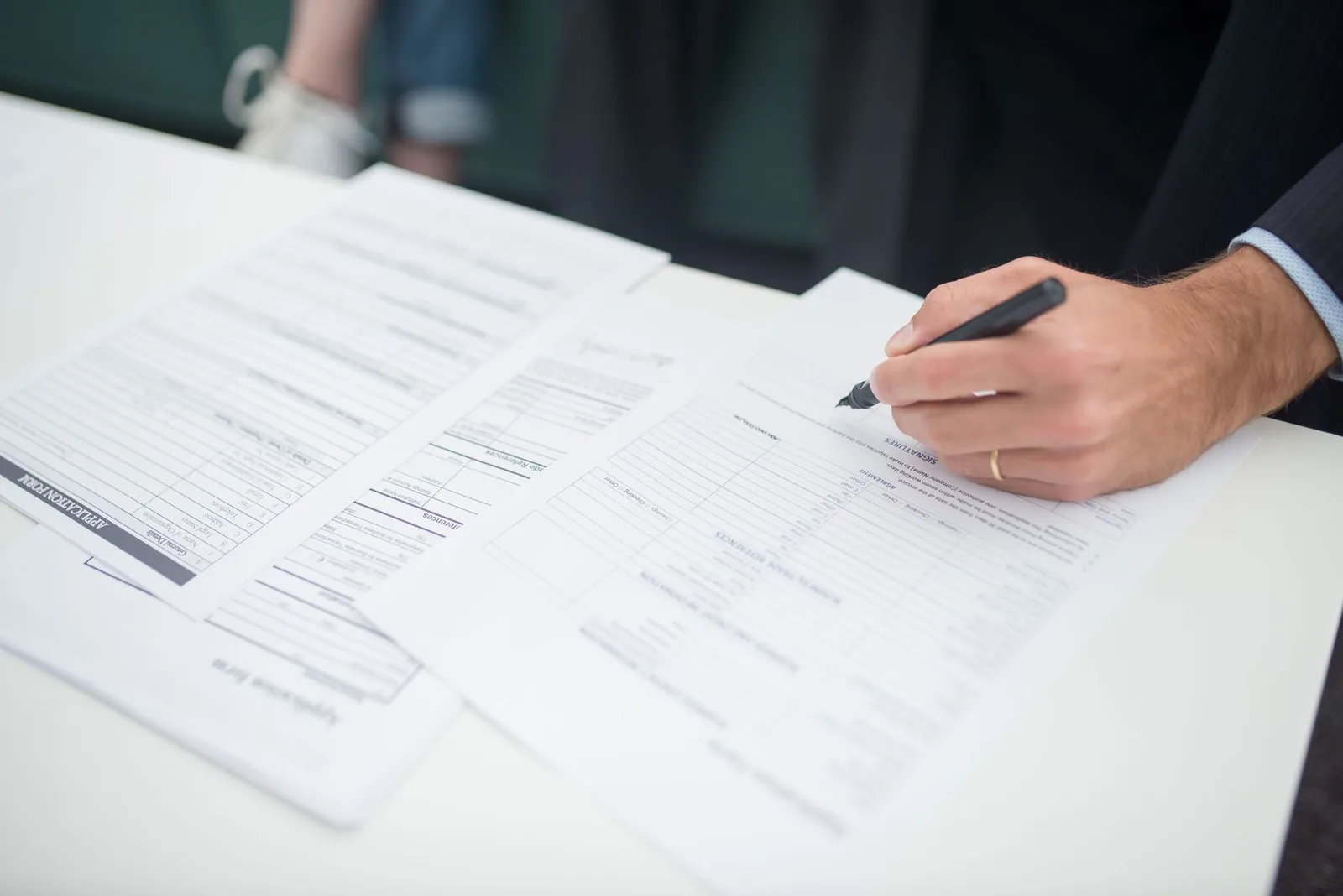 Main d'un homme signant un formulaire administratif sur une table blanche