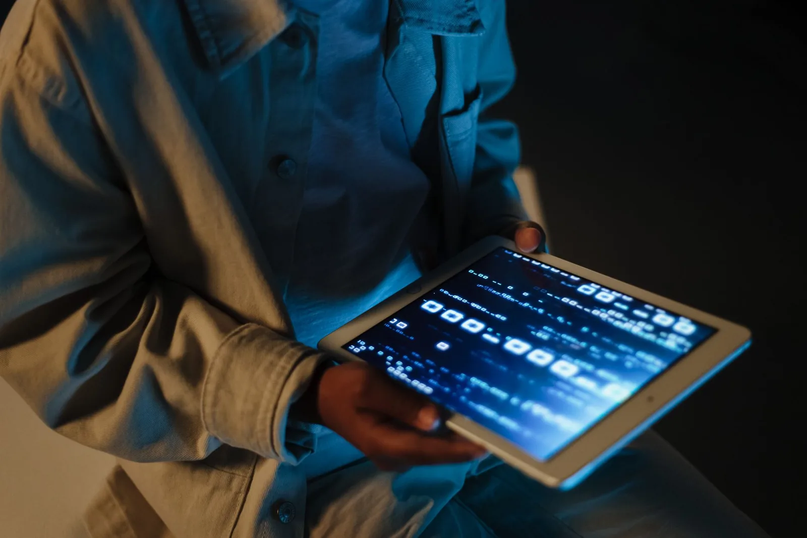 Homme tenant une tablette dont l'écran bleu affiche des données dans la pénombre