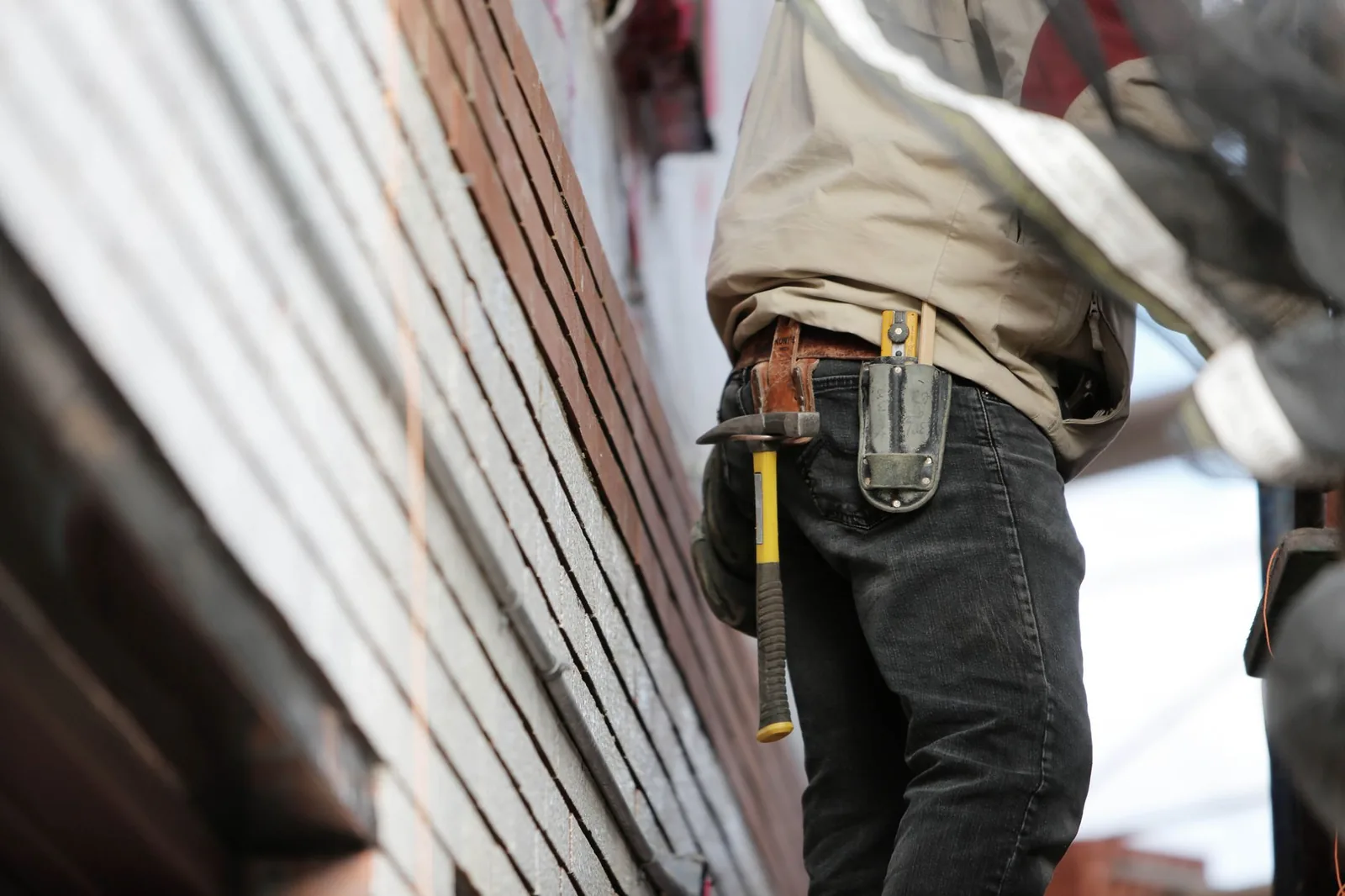 Artisan de dos portant marteau et étui à la ceinture devant un mur
