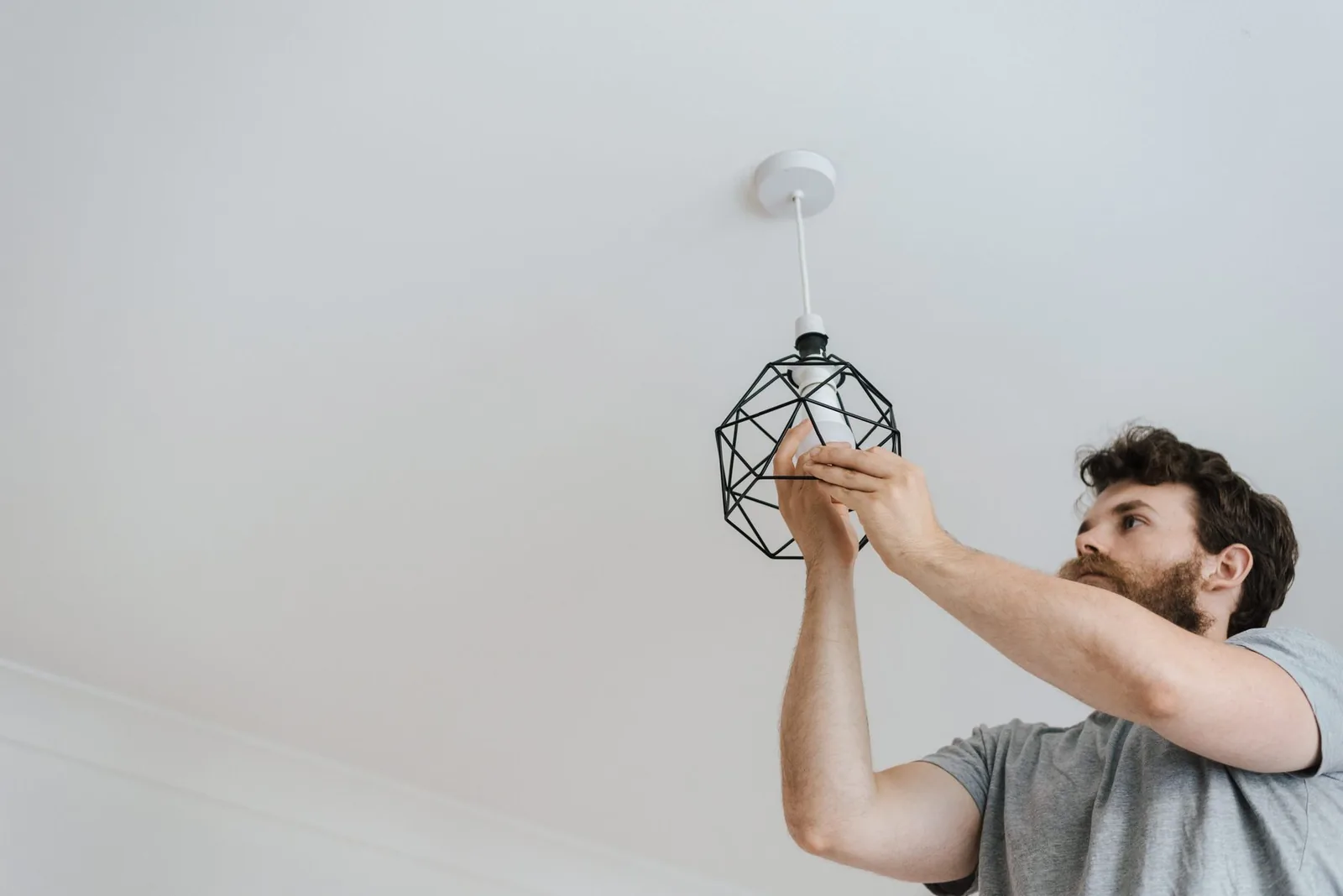 Homme changeant l'ampoule d'une suspension fixée à un plafond blanc