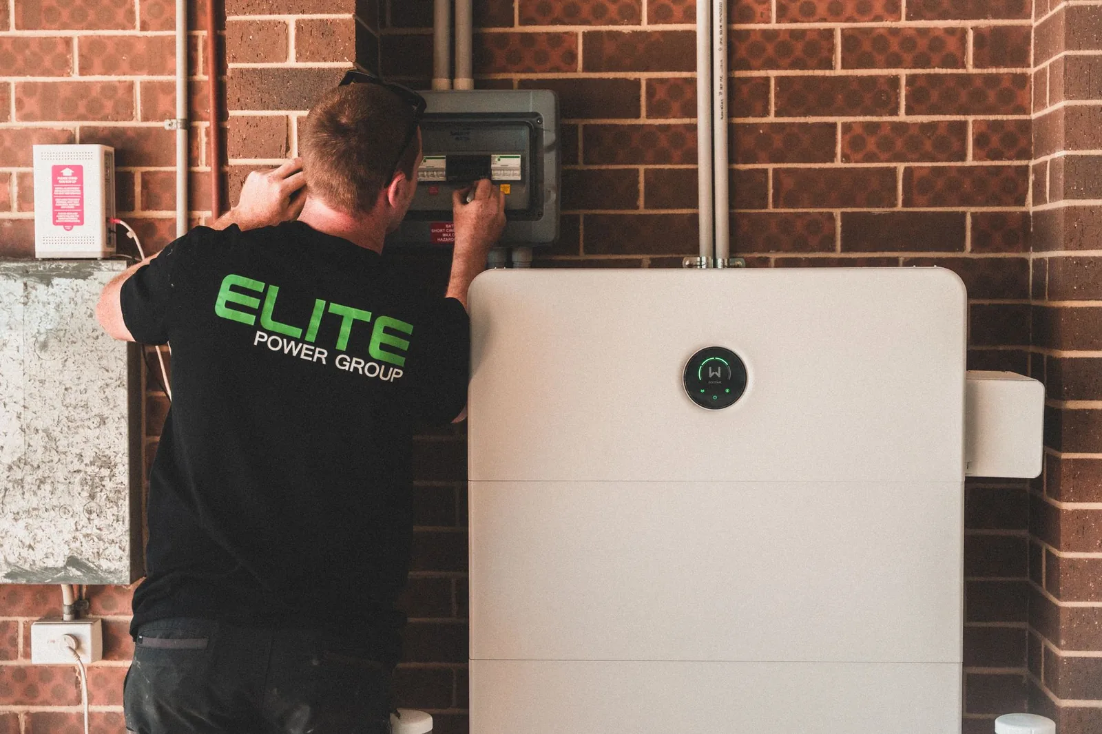 Électricien réglant un coffret électrique au-dessus d'une batterie de stockage domestique
